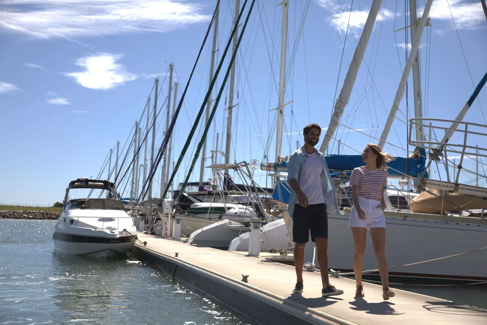 A smiling man and woman walk along the dock at Scarborough Marina on a sunny day.